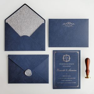 Luxury navy blue parchment wedding invitation HPI293 featuring a majestic rose gold foil stamped initial crest and border next to a matching silver glitter-lined envelope