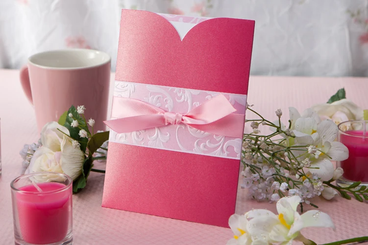 blush pink pocket wedding invitation with satin bow and embossed floral band on romantic table setting