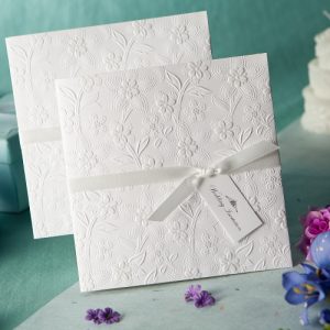Luxury white wedding invitation featuring raised floral embossing and ribbon detail