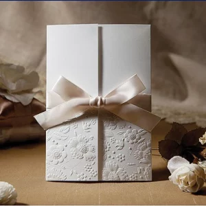 ivory embossed floral wedding invitation with champagne satin bow in elegant neutral setting