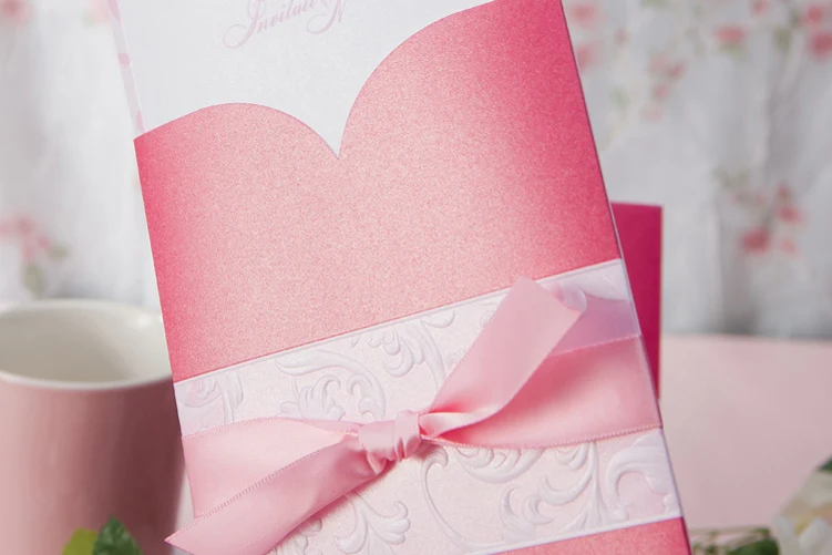 close up of pink wedding invitation with soft satin ribbon bow and embossed wrap detail
