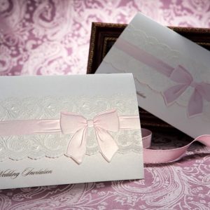 Romantic wedding invitation featuring embossed lace and pink satin ribbon pattern