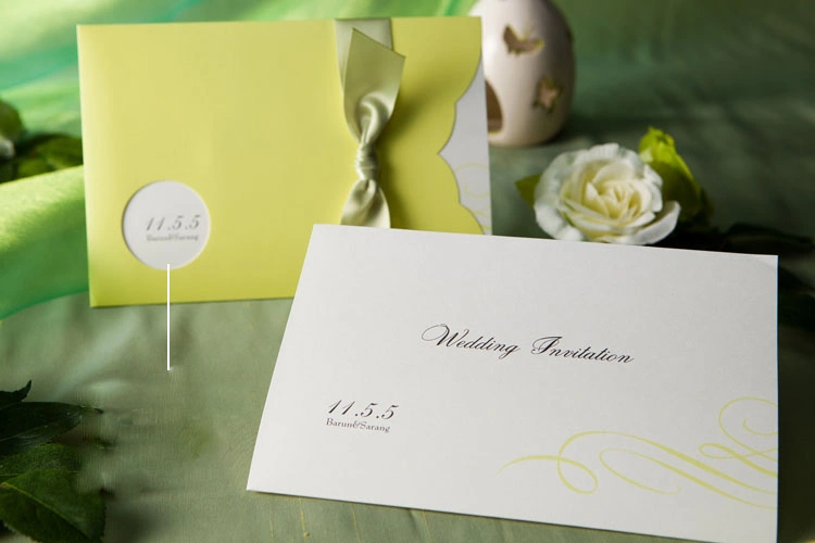 close up of pastel yellow wedding invitation with curved scalloped edge and satin ribbon bow